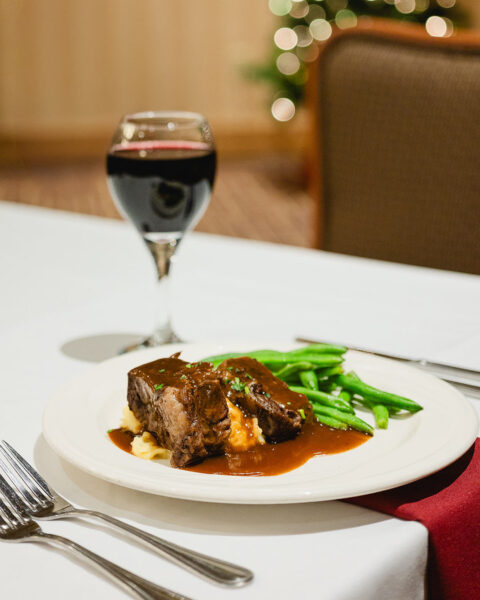 plate of meat and green beans with wine glass, forks and knives