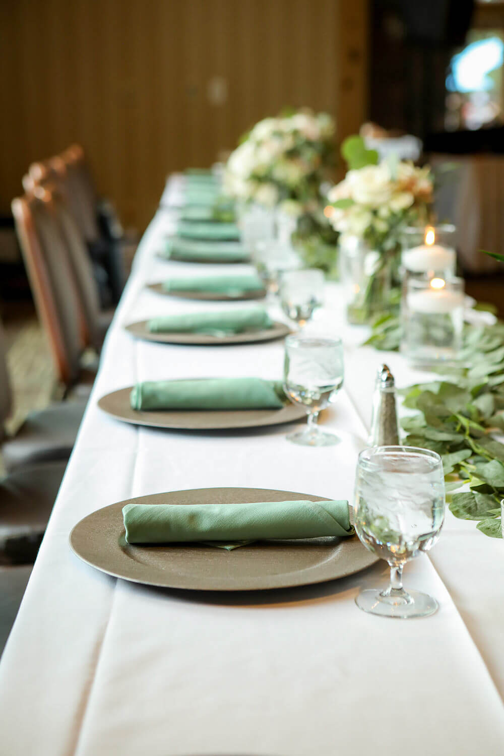 long dining table with white table cloth and plates, glasses and floral decorations