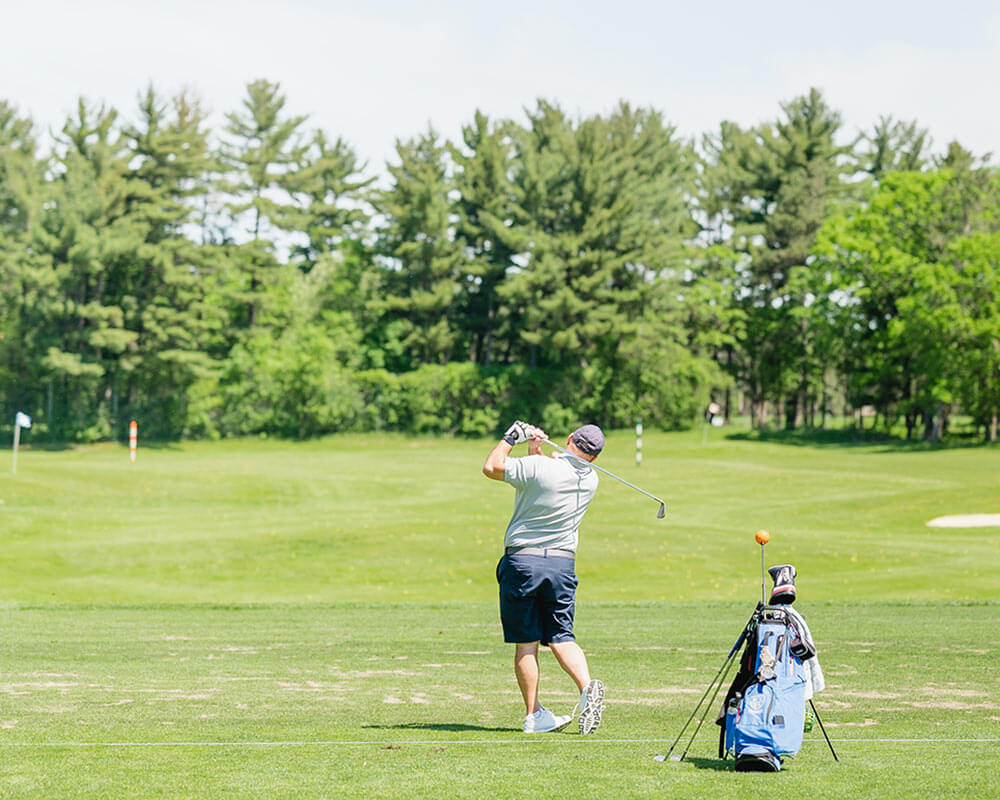golfer hitting golf ball on golf course with golf bag nearby
